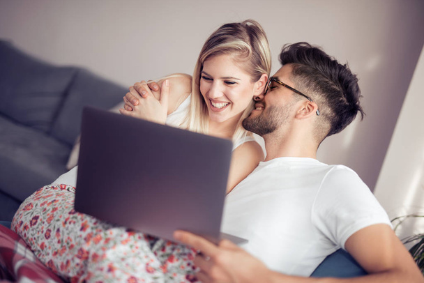 Ευτυχισμένο ζευγάρι χαλαρώνοντας μαζί στον καναπέ και να χρησιμοποιούν φορητό υπολογιστή στο σπίτι στο σαλόνι. - Φωτογραφία, εικόνα