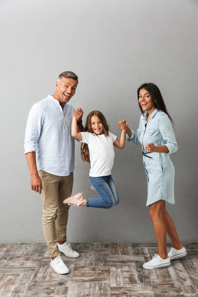 Portrait of a happy family father, mother, little daughter having fun time together isolated over gray background - Foto, afbeelding