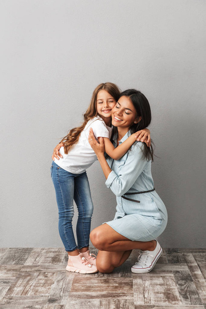 Volledige lengte beeld van gelukkige vrouw met dochter glimlachend en knuffelen elkaar geïsoleerd over grijze achtergrond - Foto, afbeelding