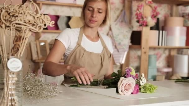 nainen kukkakauppias tekee kukkakimppu vaaleanpunaisia kukkia sisätiloissa. Nainen kukkakauppa valmistautuu kimppu ruusuja ja neilikka kukkakauppa. yrittäjyys, pienyritykset, työpaikkakäsite
.  - Materiaali, video