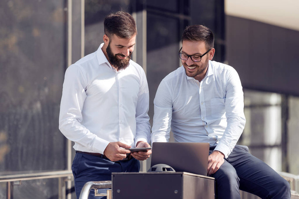 Due uomini d'affari che parlano di progetto di lavoro all'aperto, utilizzando un computer portatile
. - Foto, immagini