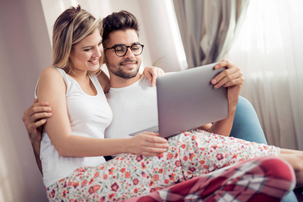 Ευτυχισμένο ζευγάρι χαλαρώνοντας μαζί στον καναπέ και να χρησιμοποιούν φορητό υπολογιστή στο σπίτι στο σαλόνι. - Φωτογραφία, εικόνα