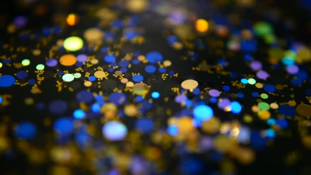 Defocused shimmering multicolored glitter confetti, black background. Holiday abstract festive bokeh light spots. - Footage, Video