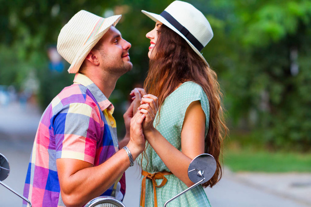 Молода щаслива пара в любові катається на старовинному скутері на вулиці в капелюхах. Концепція відпочинку та подорожей
 - Фото, зображення