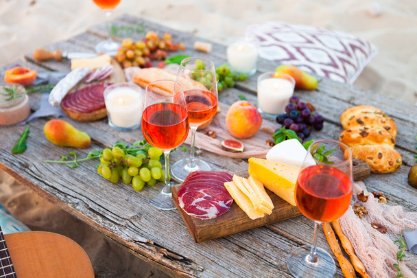Picnic on the beach at sunset in boho style. Romantic dinner, friends party, summertime, food and drink conception - Zdjęcie, obraz