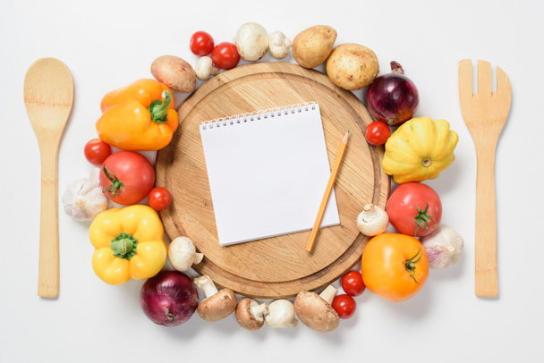 vista superior de verduras maduras alrededor de tablero de madera, cuaderno y lápiz aislado en blanco
 - Foto, Imagen