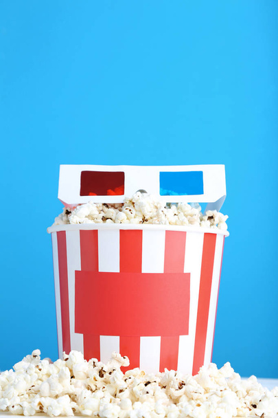 Popcorn in striped bucket with glasses on blue background - Foto, imagen
