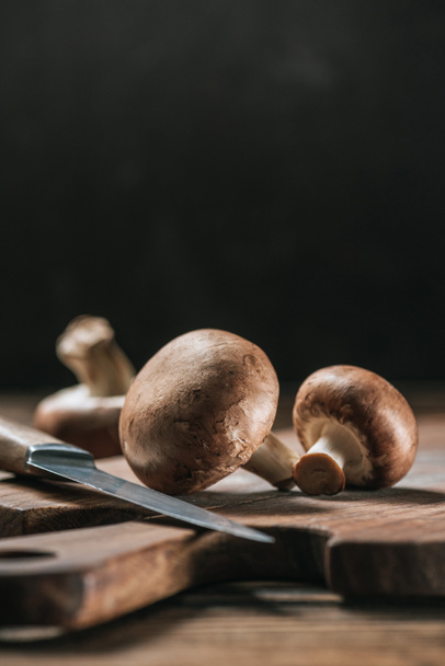 ripe portobello mushrooms and knife on wooden table isolated on black - Foto, afbeelding