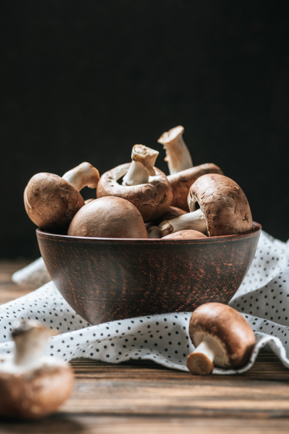 ripe champignon mushrooms in bowl on wooden table isolated on black  - Фото, изображение