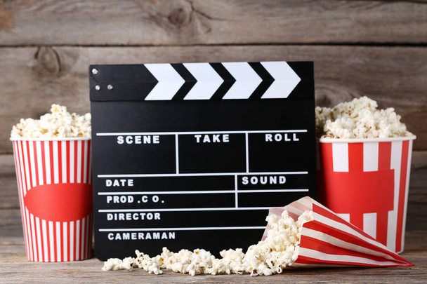 Clapper board with popcorn in striped buckets on wooden table - Photo, image