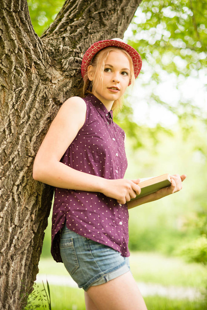 όμορφη νεαρή ξανθιά κοπέλα με καπέλο και πουκάμισο σε φόντο φύση  - Φωτογραφία, εικόνα