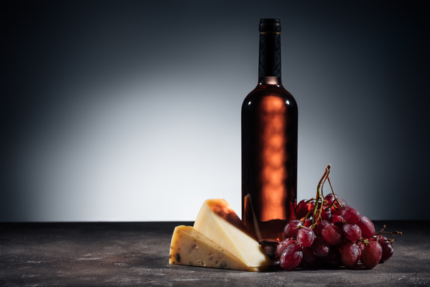 pullo punaviiniä, erityyppisiä juustoja ja rypäleitä puupöydällä
 - Valokuva, kuva