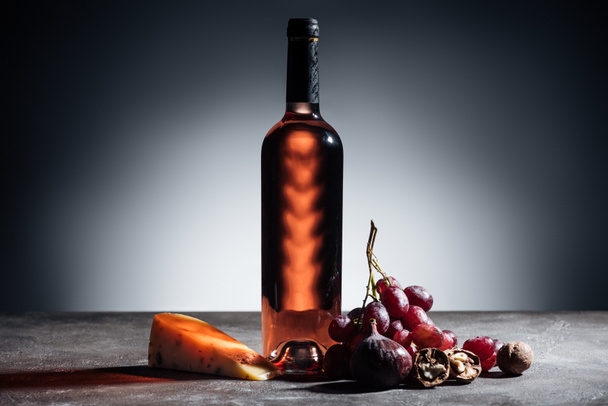 bottle of red wine, piece of cheese and grapes on grey - Fotografie, Obrázek