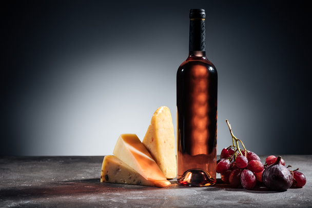 μπουκάλι κόκκινο κρασί, διάφορα είδη νόστιμα τυριά και σταφύλια σε γκρι - Φωτογραφία, εικόνα