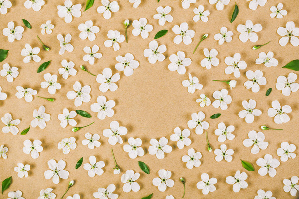 Floral frame made of white spring flowers, buds and green leaves on brown paper background. Flat lay. Top view. - Photo, Image