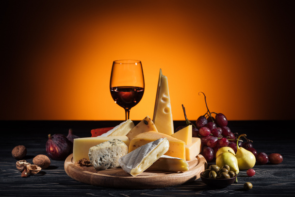 different types of cheeses, wineglass and fruits on table on orange - Photo, Image