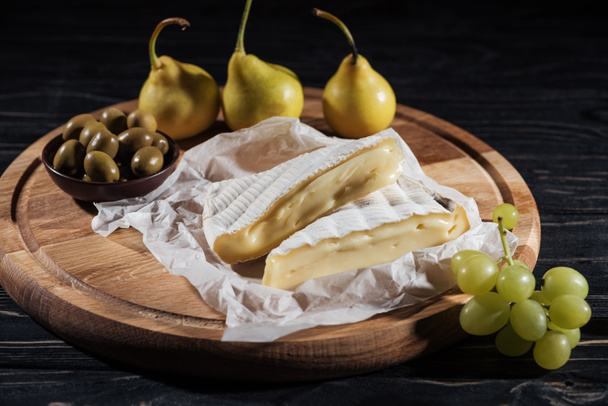 köstlicher Brie-Käse, Trauben, Birnen und Oliven auf Schneidebrett - Foto, Bild