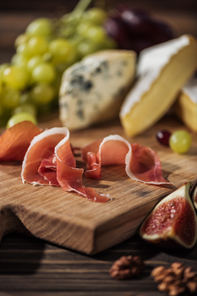 prosciutto on cutting board with cheeses on background - Photo, Image