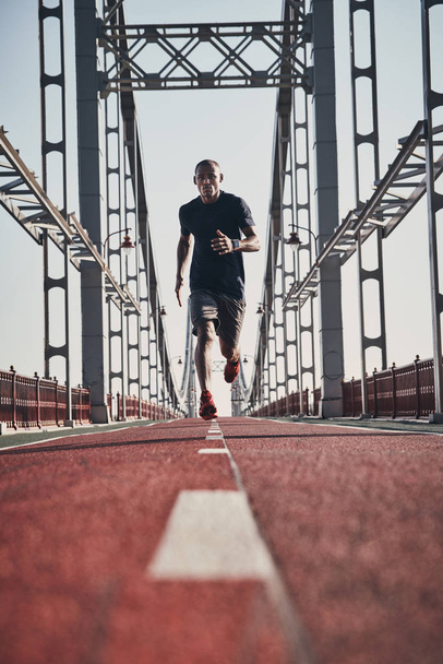 African man in sports clothing exercising and jogging on bridge outdoors - Valokuva, kuva