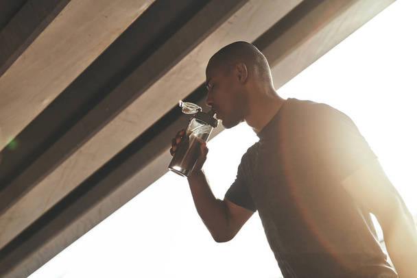 Young African man in sports clothing drinking water while standing outside under bridge  - Fotoğraf, Görsel