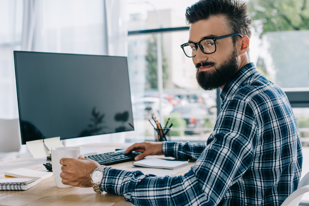young successful seo sitting at workplace with blank computer screen and looking at camera - Photo, Image