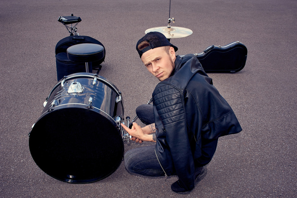 Drummer in zwarte kleding wijzend op Drumstel op straat - Foto, afbeelding