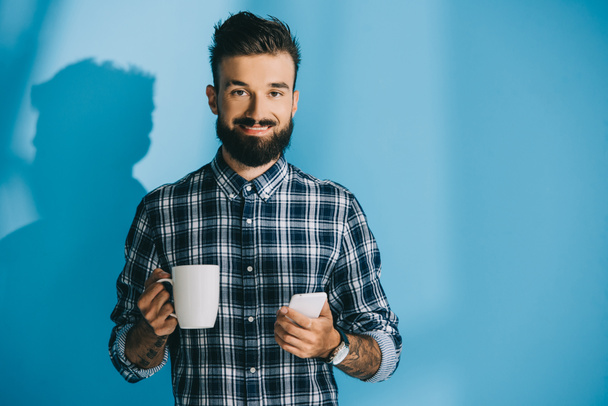 smiling man in checkered shirt holding smartphone and cup of coffee - Fotoğraf, Görsel