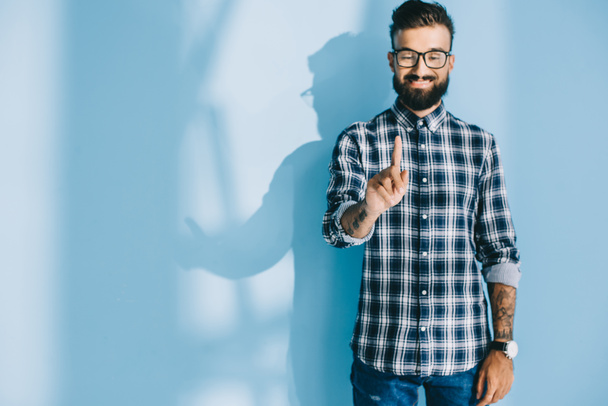 smiling bearded man in checkered shirt pointing at something, on blue - Φωτογραφία, εικόνα