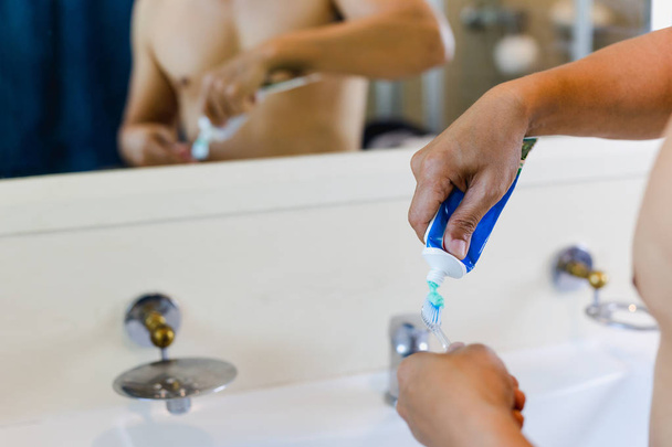 Adam evde banyoda diş fırçası içine diş macunu sıkma. - Fotoğraf, Görsel