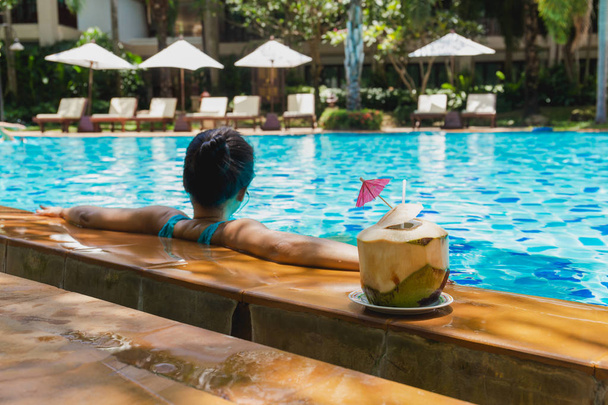 Woman relax having coconut drink and listen to music in swimming pool on vacation. - Photo, Image