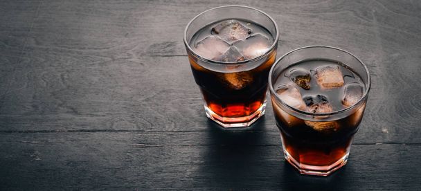 Whiskey with ice in a glass. Rum-Cola. Brandy. On a black wooden background. Top view. Free space for text. - Φωτογραφία, εικόνα