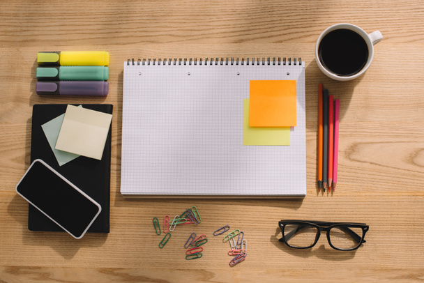 top view of office supplies, stick notes, smartphone, paper clips, notebook and cup of coffee - Foto, Imagen