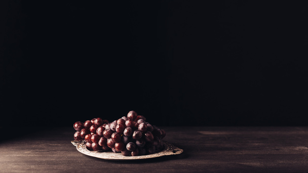 fresh ripe red grapes on vintage plate on wooden table on black - Foto, afbeelding