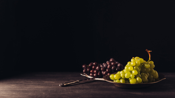 uvas rojas y blancas maduras frescas en platos y cuchillo vintage en mesa de madera sobre negro
 - Foto, imagen