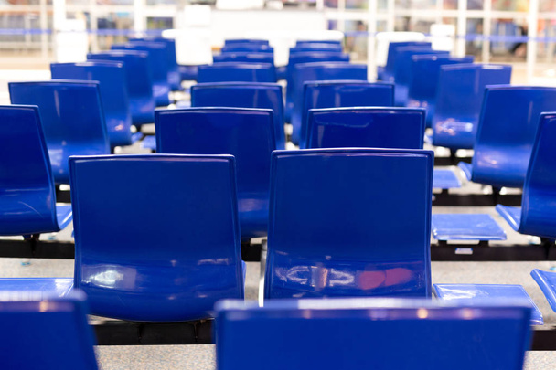 Sininen lentokenttätuoli, jossa hämärtyneet ihmiset istuvat ja odottavat lähtöä lentokentän terminaalissa
. - Valokuva, kuva