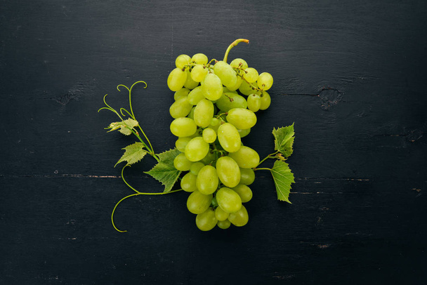 Fresh green grapes with leaves of grapes. Top view. On a black wooden background. Free space for text. - Photo, Image