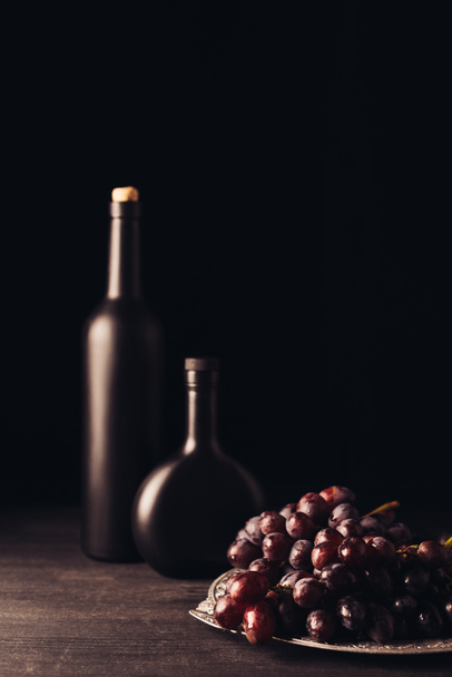fresh ripe red grapes and bottles of wine on wooden table on black   - Foto, Imagem