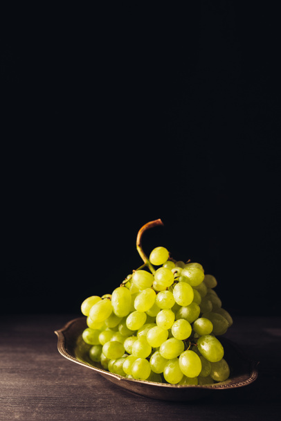 close-up view of fresh ripe white grapes on vintage plate on wooden table on black  - Foto, Bild