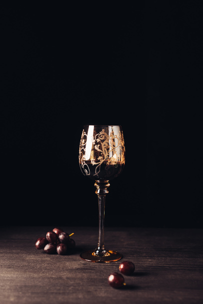 glass of delicious red wine and fresh grapes on wooden table on black - Foto, Bild