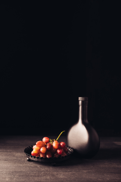 fresh ripe red grapes and bottle of wine on wooden table on black - Фото, зображення