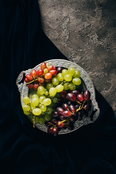 top view of various types of grapes on vintage plate on dark fabric - Foto, afbeelding
