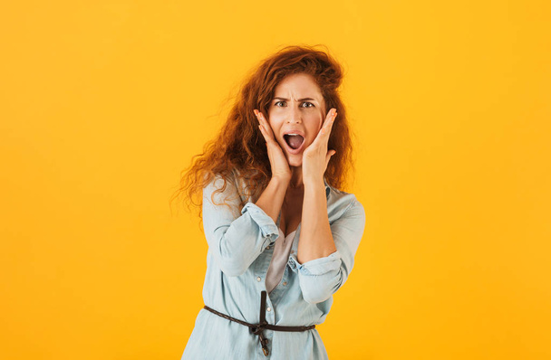 Thrilled emotional woman 20s holding hands at face and screaming isolated over yellow background - Foto, Imagen
