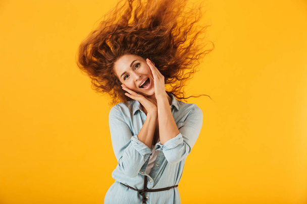 Image of caucasian cheerful woman 20s with shaking hair holding hands at face and smiling isolated over yellow background - 写真・画像