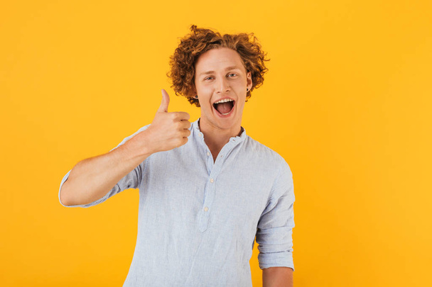 Image of european happy guy 20s smiling and showing thumb up at camera isolated over yellow background - Foto, immagini