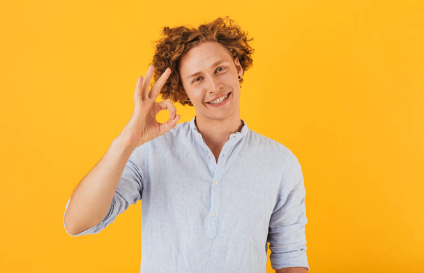 Photo of pleased cheerful guy 20s smiling and showing ok sign at camera isolated over yellow background - Fotoğraf, Görsel