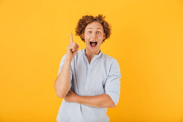 Photo of amazed young man 20s screaming and pointing finger upward at copyspace isolated over yellow background - Foto, imagen