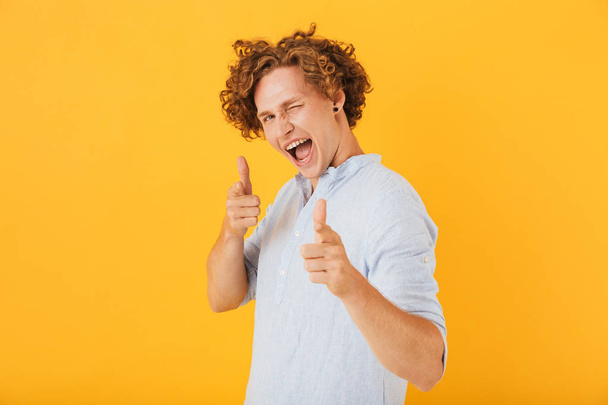 Image of european flirty guy 20s laughing and pointing finger at you isolated over yellow background - Foto, imagen