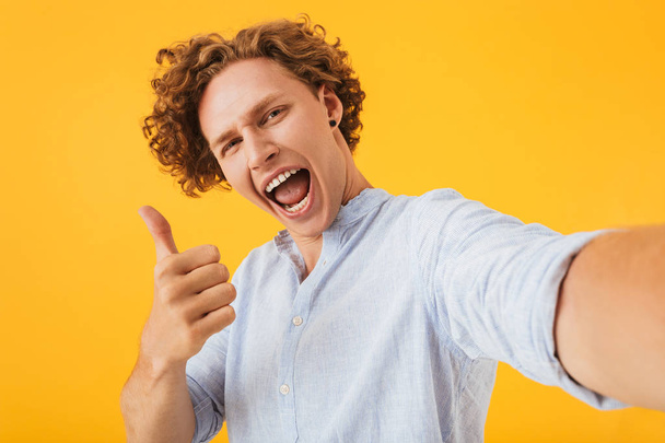 Photo of caucasian joyous man 20s taking selfie photo and showing thumb up isolated over yellow background - Valokuva, kuva