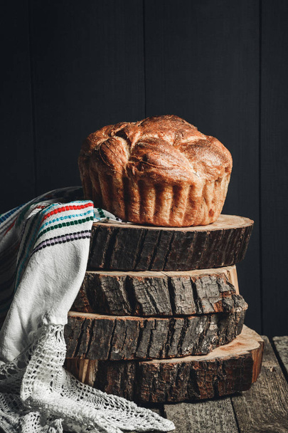 Свежеиспеченный буханка хлеба на темном деревянном фоне, пни и ткань. Пасхальный хлеб
. - Фото, изображение