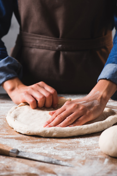 partial view of woman in apron kneading dough for pizza - Foto, afbeelding